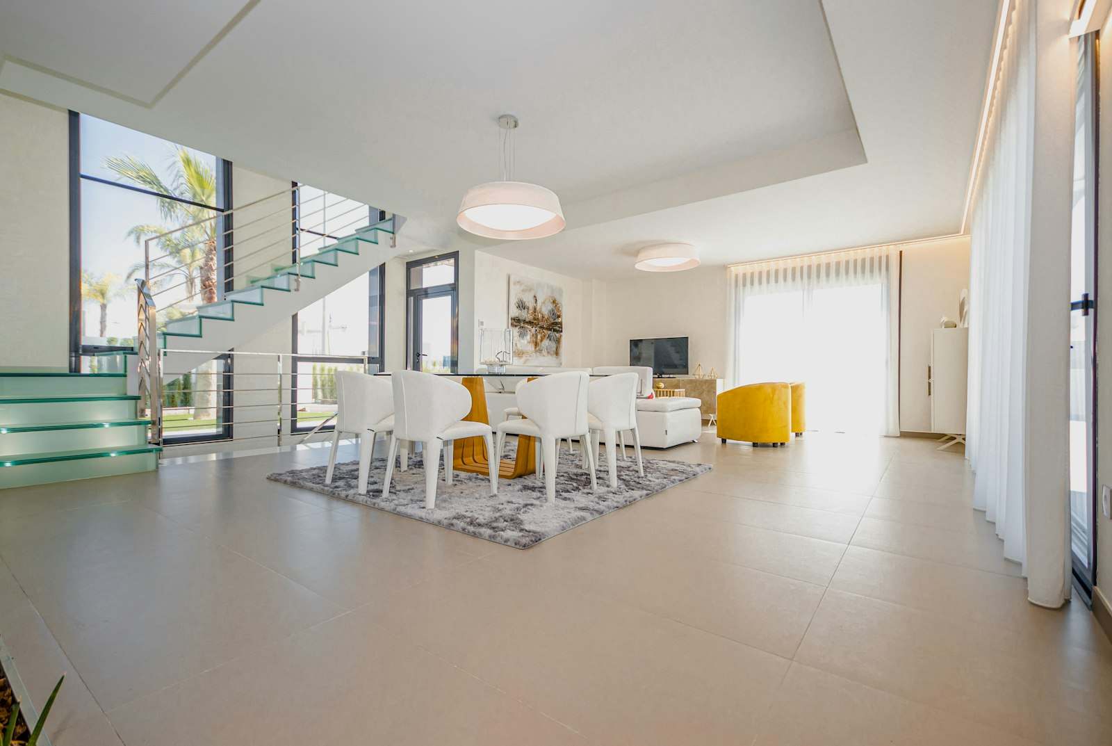 Interior de villa luminoso con salón y comedor abiertos y escalera de cristal